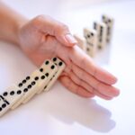 A hand stopping the domino effect, captured on a white background, symbolizing control.